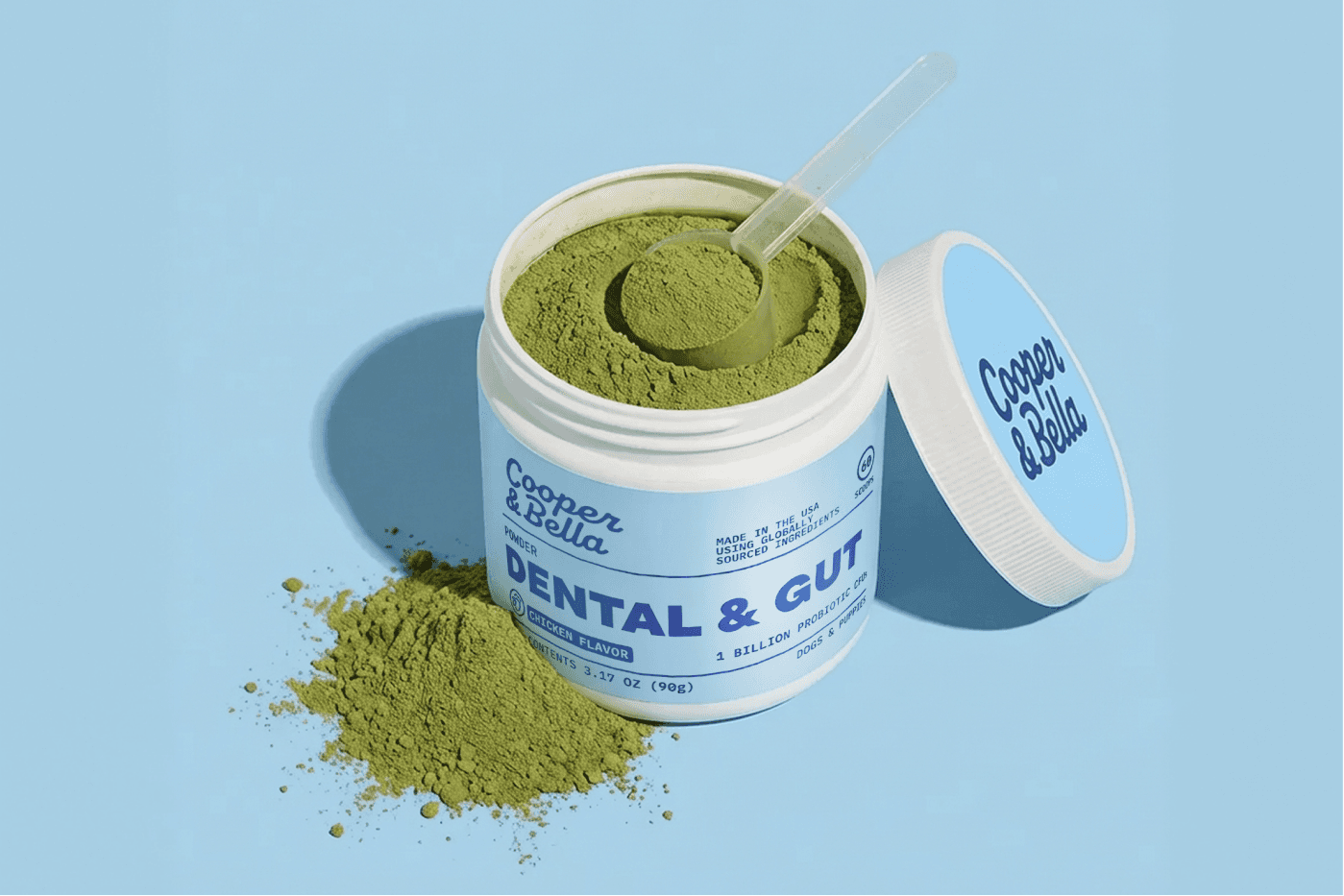 Cooper & Bella Dental & Gut jar open with scoop and green powder on a blue background